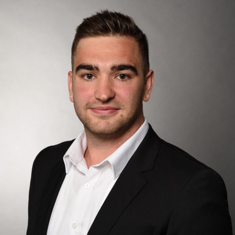 Business Portrait Robin Dietrich Junger Mann im Anzug mit weißem Hemd und kurzem, braunem Haar, neutraler Hintergrund.