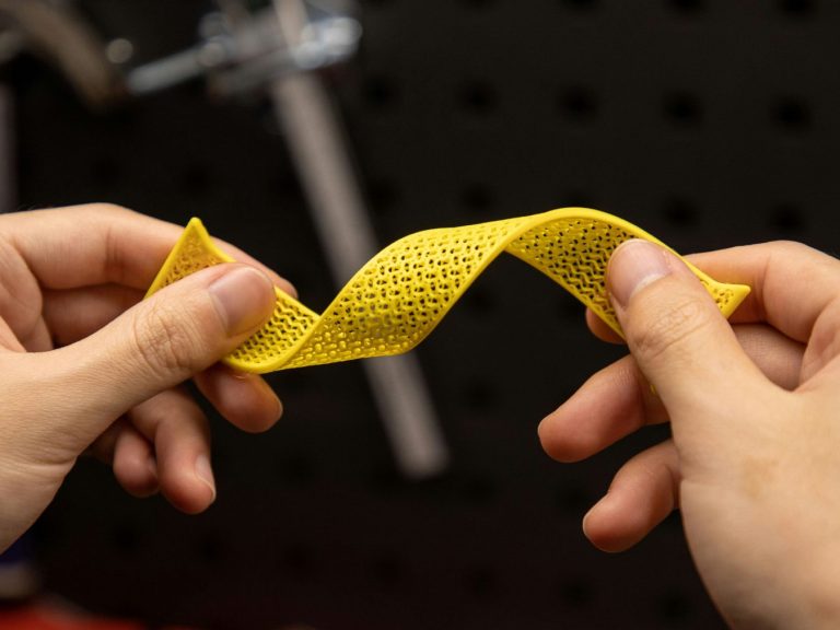 Flexible Elastomere Eine Person hält ein gelbes, gewundenes Stück Material zwischen den Händen und tordiert es.